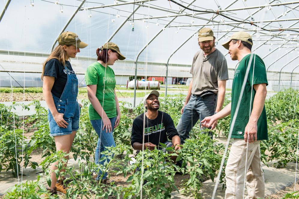 group of students and staff smiling in the greenhouse working with plants