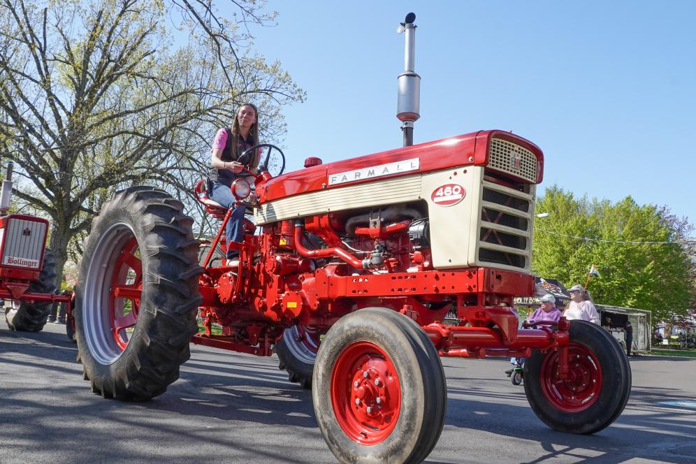 A student is riding a large red tractor on main campus. 