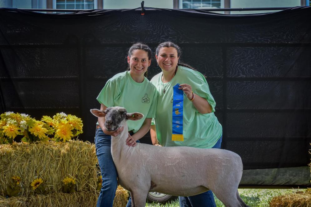 Two students hold up a ribbon they won for a livestock show. 