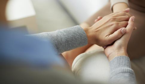 Two people hold hands in a counseling or support meeting.