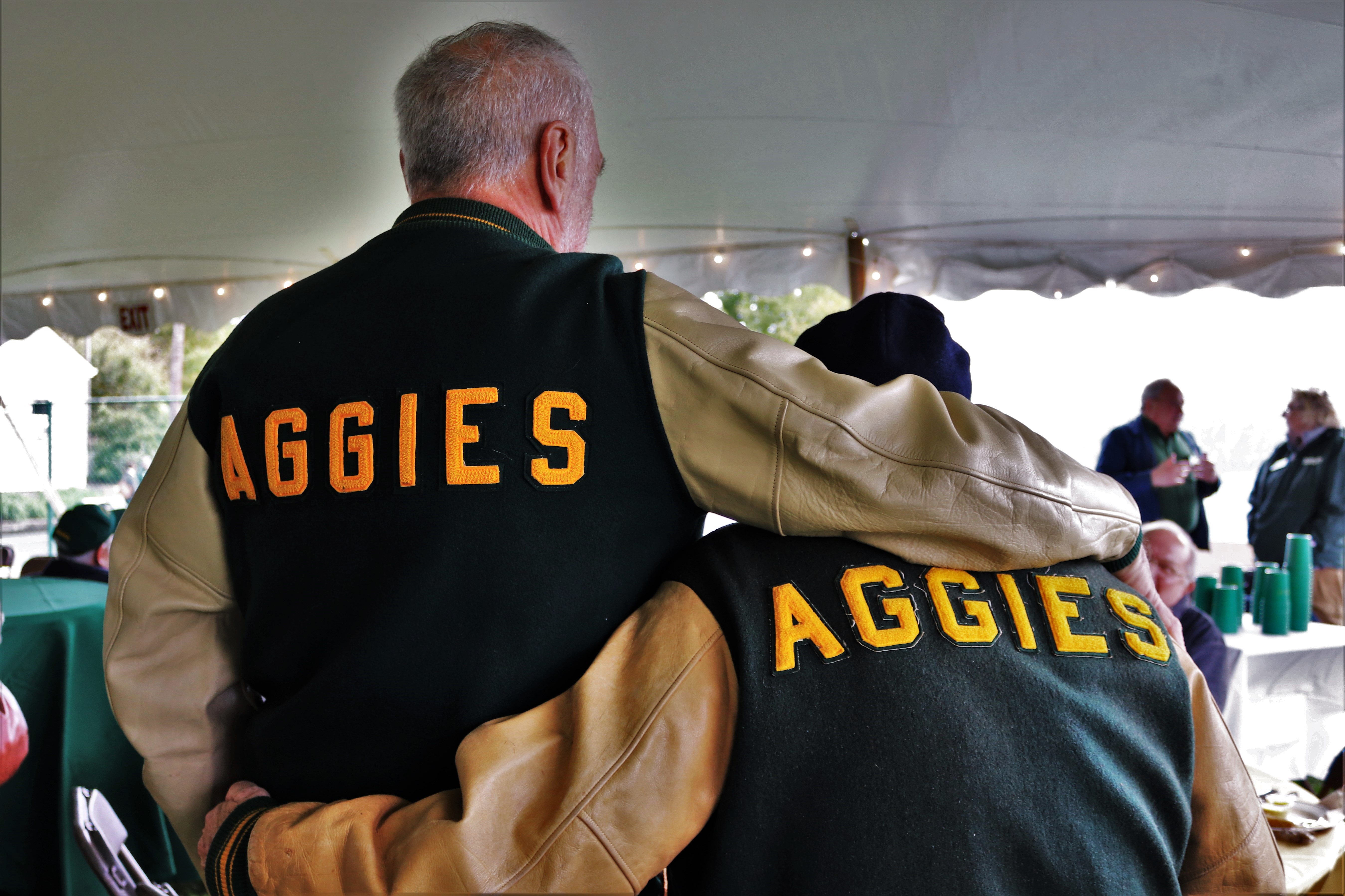 Two alumni embracing wearing Aggies leterman jackets 