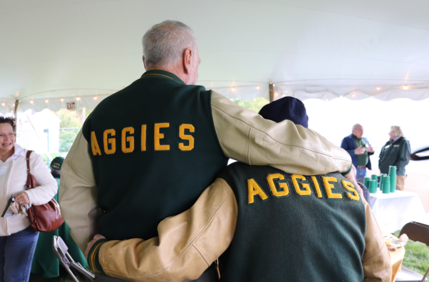 Two alumni wearing vintage "aggies" jackets are hugging. 