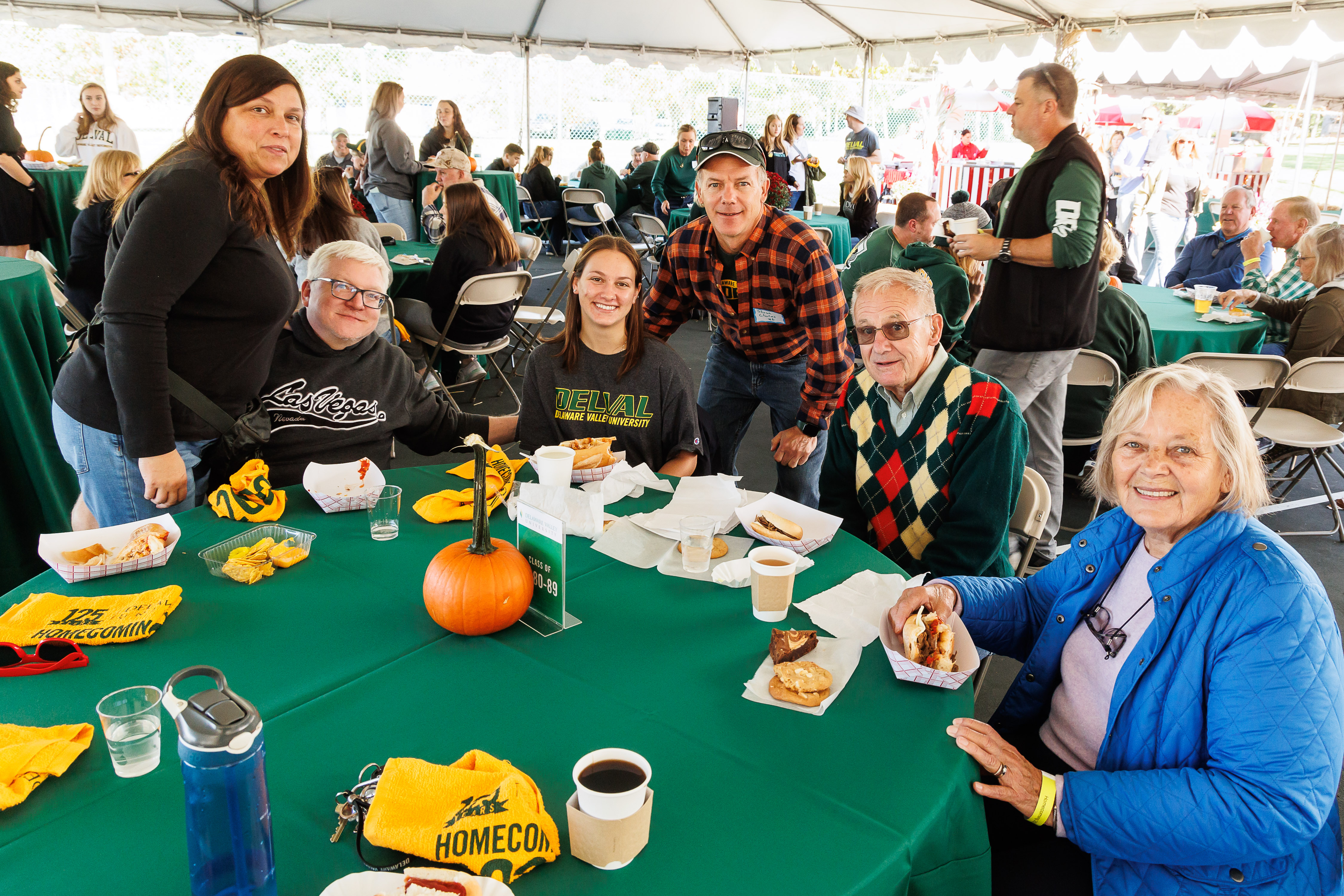 Alumni are seated at a table during homecoming with food and refreshments. 