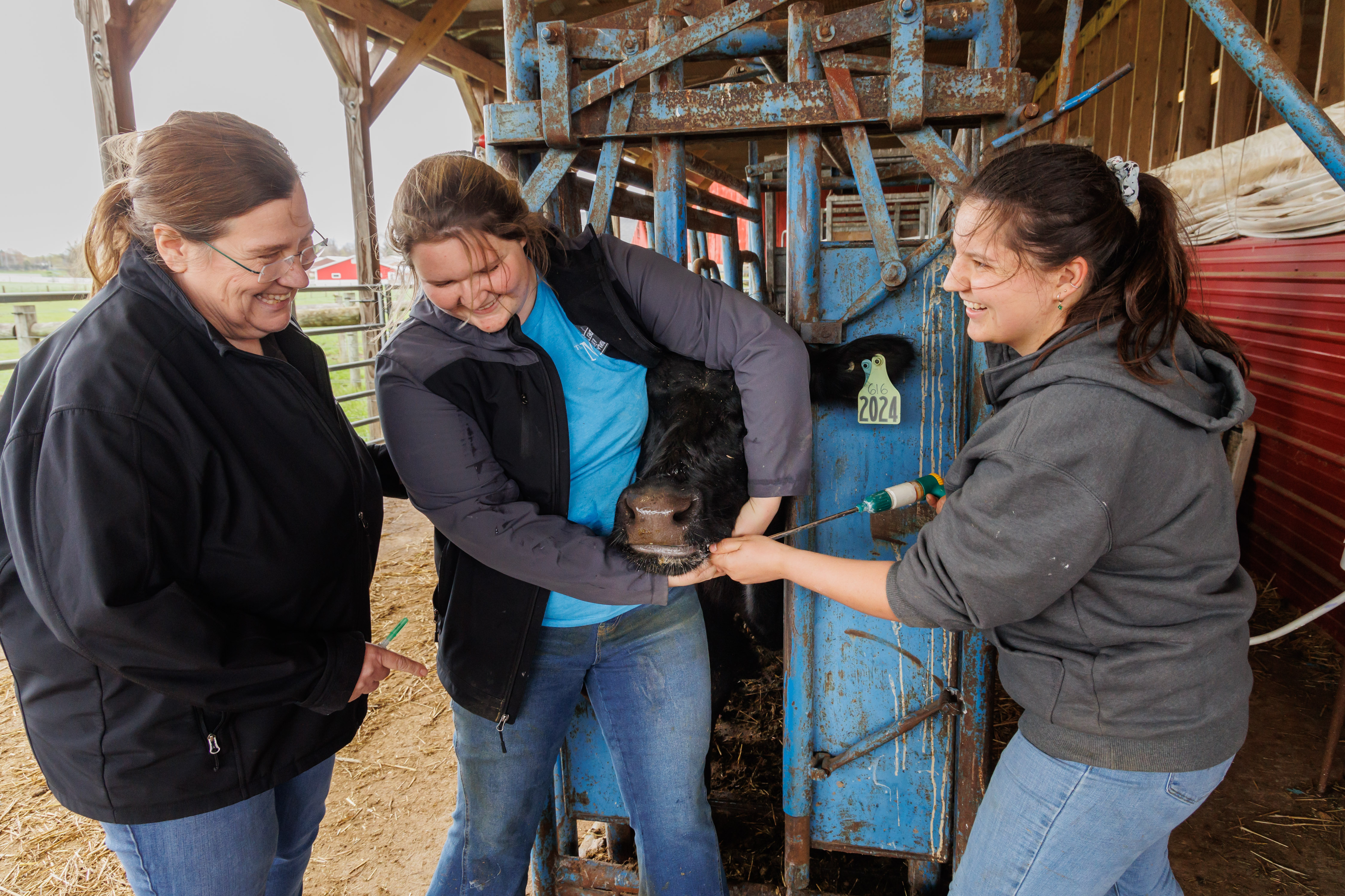 Two female students are in the dairy barn learning from Joanne Powell. 