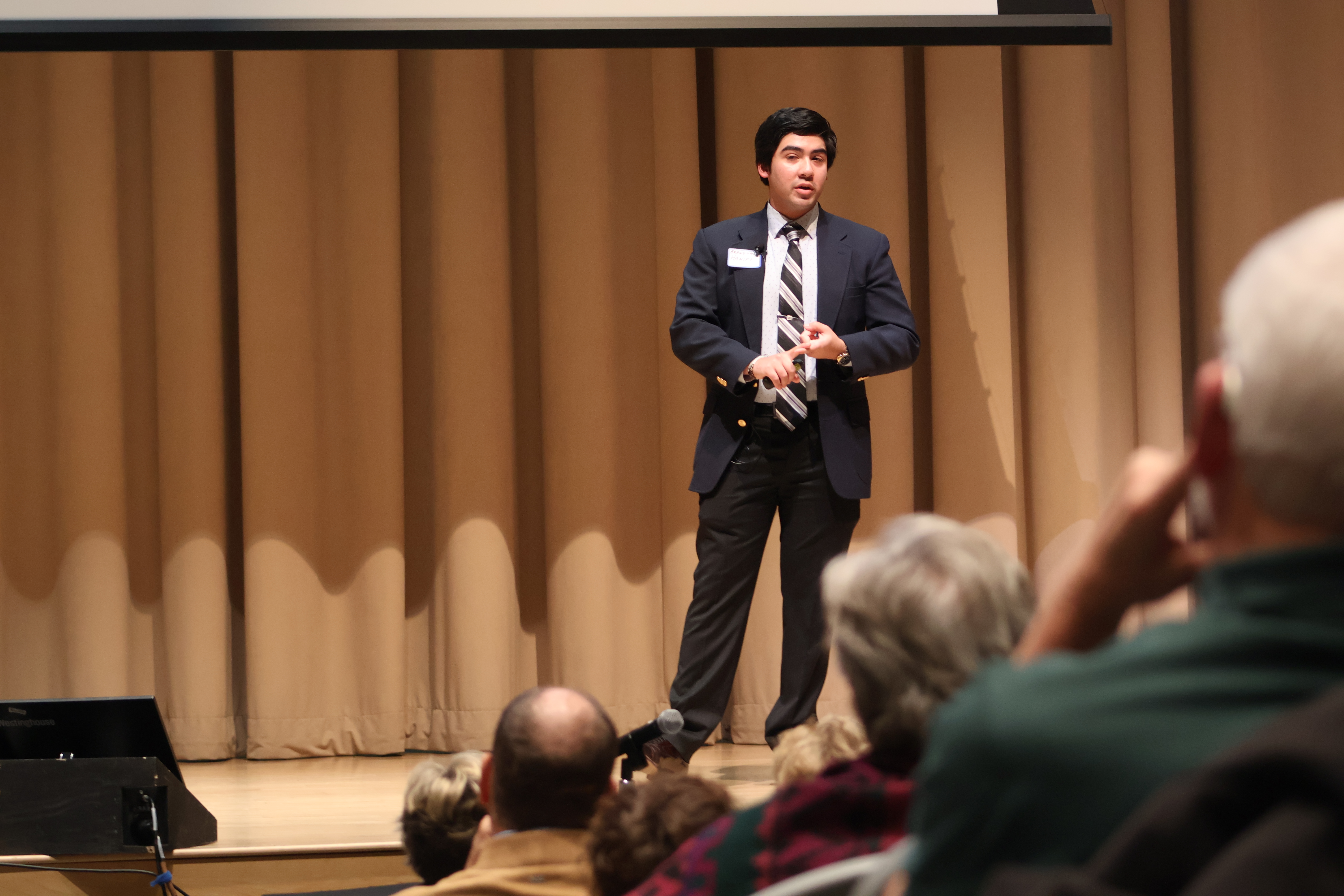 A student dressed in business attire is on a stage pitching a business idea at our annual spark bowl event. 