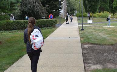 A student is walking on a scenic campus path wearing a backpack. 