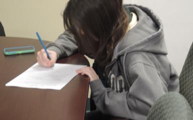 A student sits alone at a table and completes an assignment.