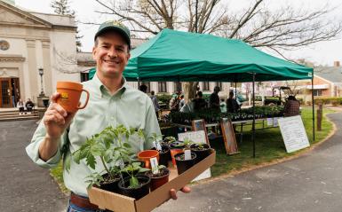 A man holding a delval mug and plants in front of athe horticulture tent at a-day. 