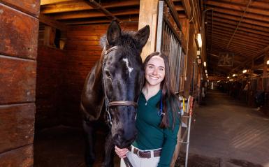 A DelVal Alumna is standing and holding the face of a horse inside the equestrian center.