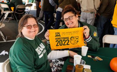 Two smiling alumni holding up DelVal printed towels from homecoming 2022. 