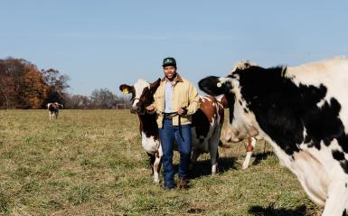 Darian Poles'21 is walking in the field with cows. 