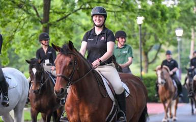 Several students are riding horses on campus. 