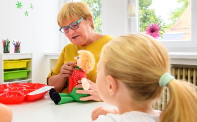 A speech language pathologist is pointing to the mouth of a doll to teach speech techniques.