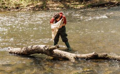 A student is outdoors by a creek holding a net. 