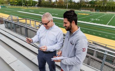 A student and professor are on the field in the stadium. 