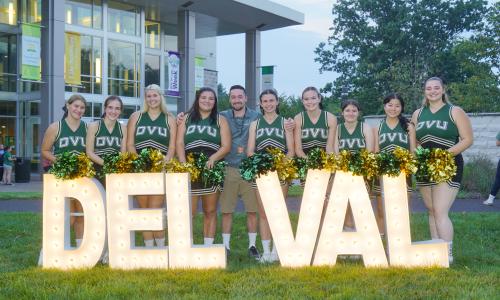 DelVal cheerleaders stand with a light up DelVal sign on campus.
