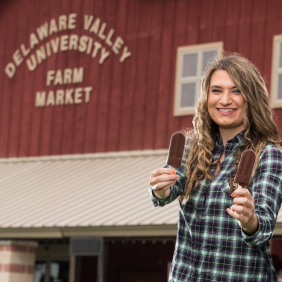 Margaret Gadomski standing in front of the Market at DelVal holding two ice cream popsicles.