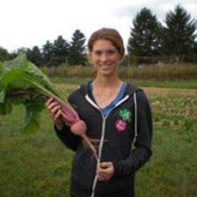 Johanna Baglivi, a 2015 graduate, holding a large turnip in a planted field