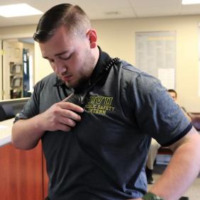 Chris George, a criminal justice major, uses a radio in the public safety office on campus while wearing a grey collared shirt.
