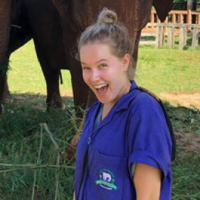 Student in scrubs smiling in front of two elephants.