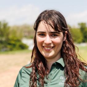 A headshot of jaclyn fiola wearing a delval green collared shirt in a field of soil. 