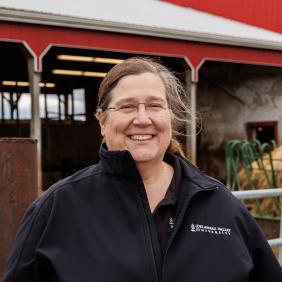 Joanne Powell headshot by the dairy barn, wearing a black delval zip up jacket. 