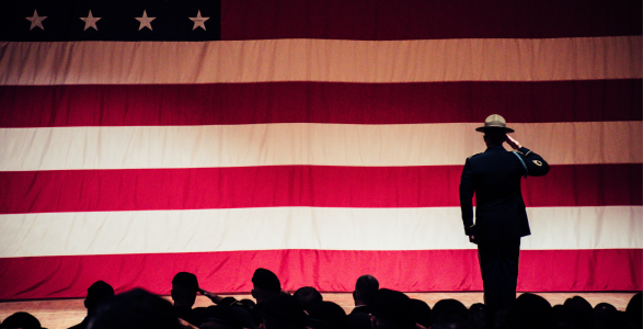 A veteran stands in front of an american flag. 