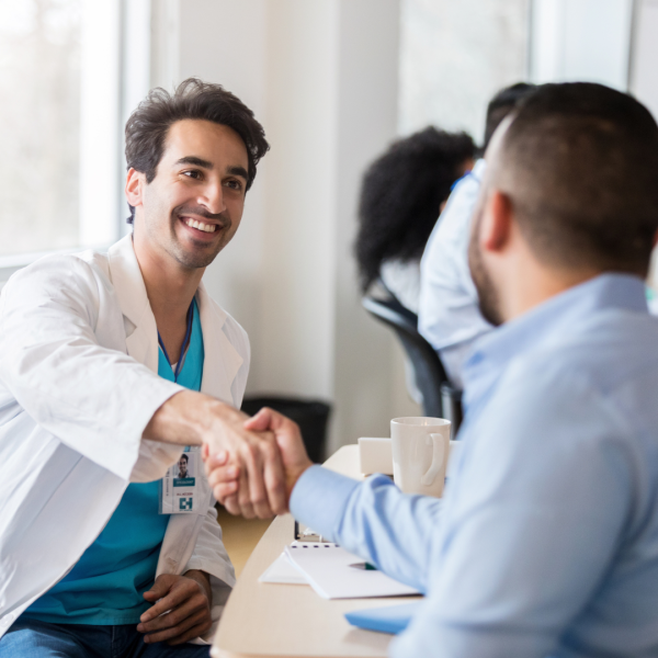 A male doctor is shaking a businessman's hand in an office setting. 