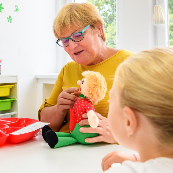 A speech language pathologist is pointing to the mouth of a doll to teach speech techniques.