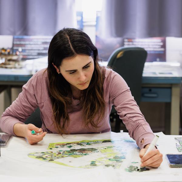 A landscape architecture student is drawing on large paper in the design studio. 