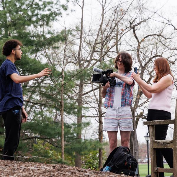 A professor and two students are outside working with a large video camera. 
