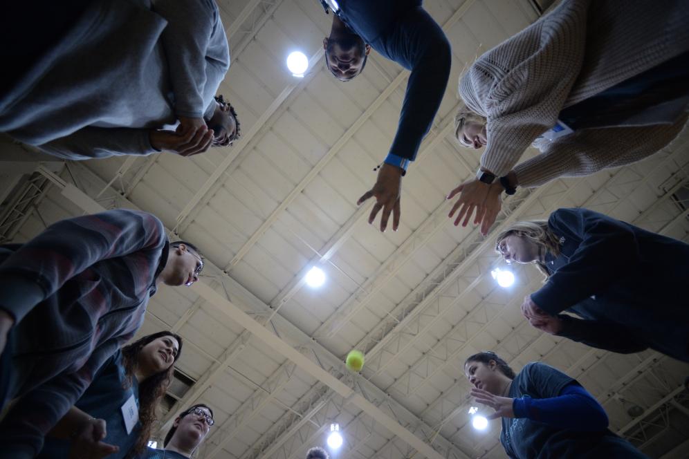 group of students tossing a tennis ball in a circle