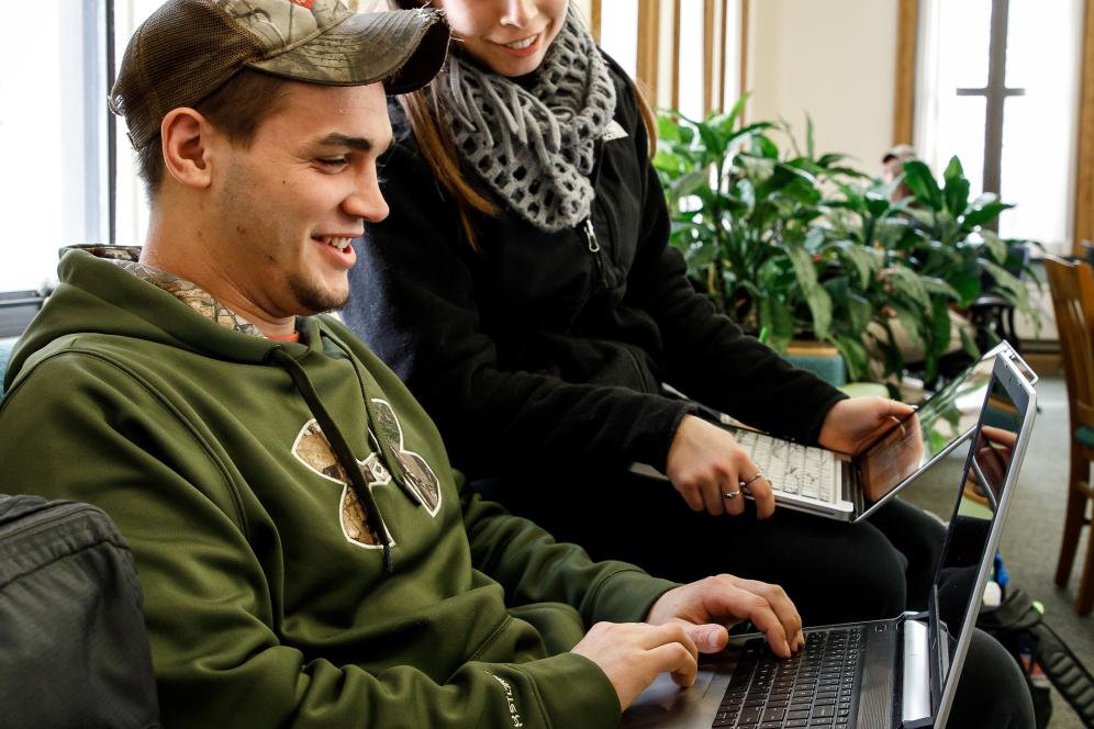 Two students looking at a laptop in the library. 