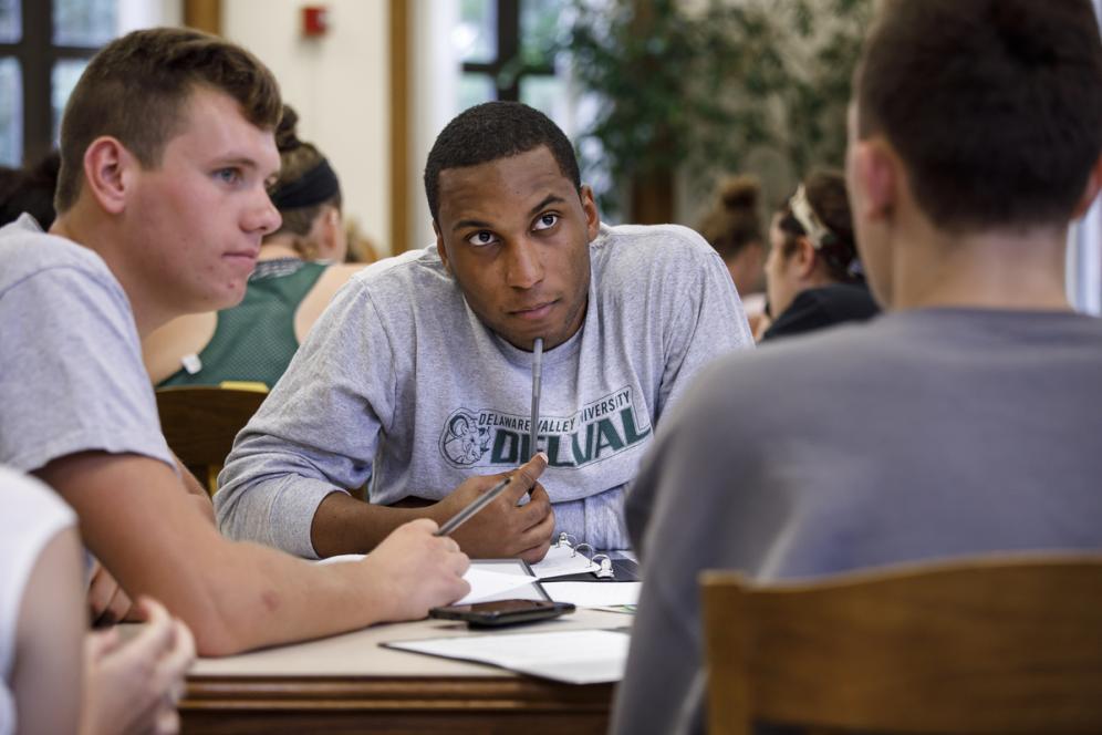 Three students participate in a discussion at a table during a workshop for student-athletes on using their experiences on the field in their job search process.