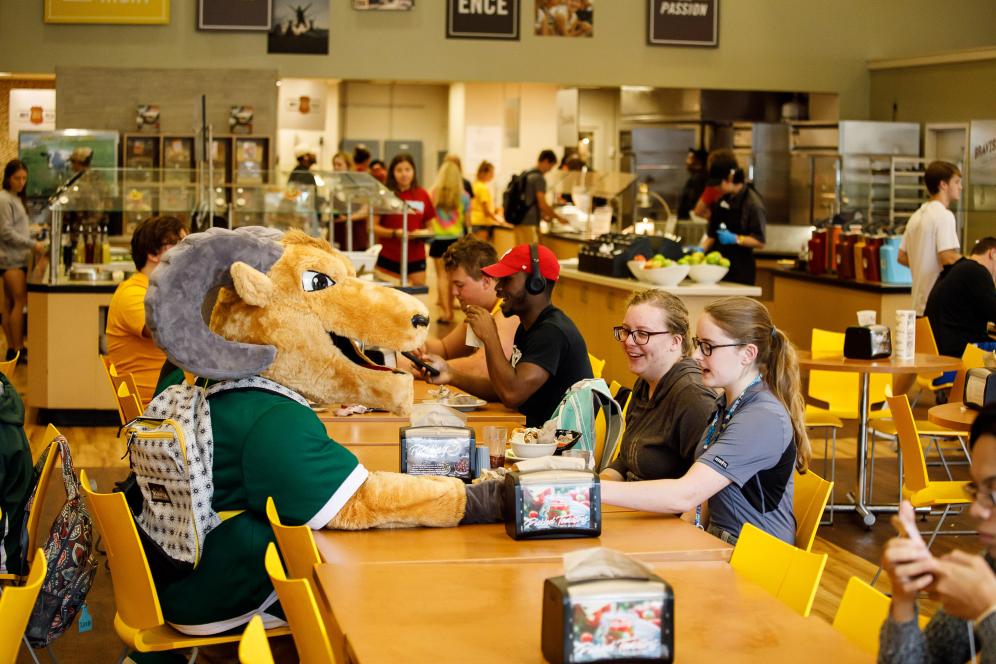 The mascot sitting at the lunch table with two students.