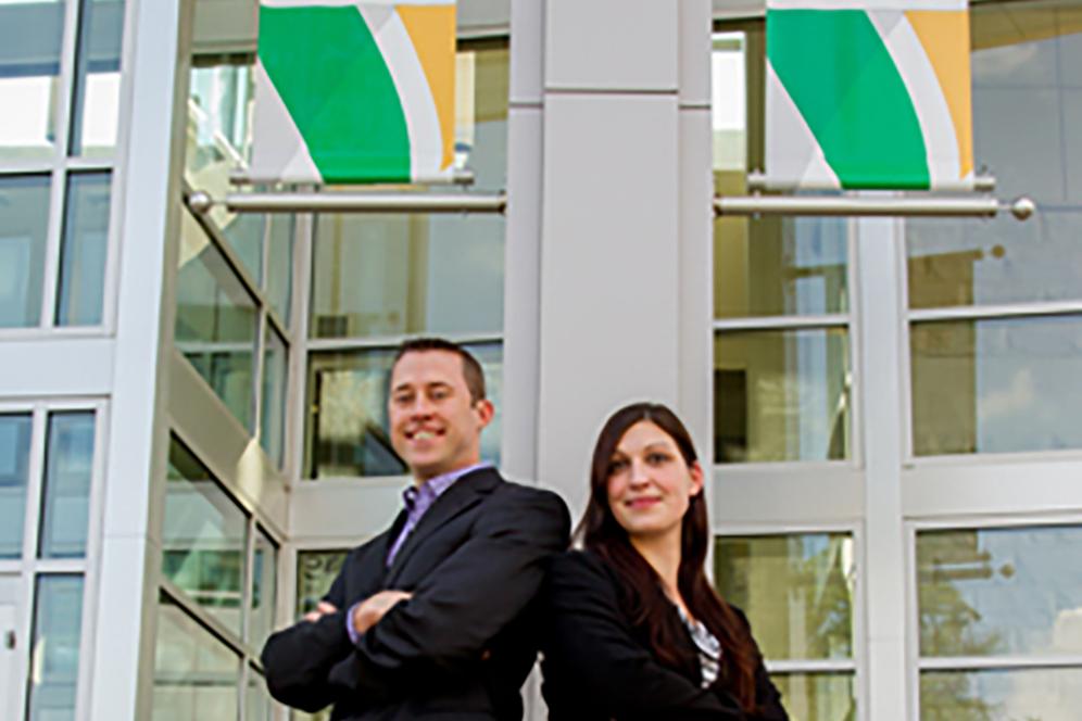 Two students in business dress in front of glass building.