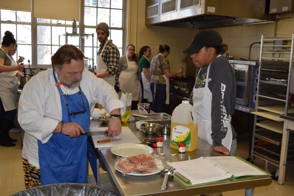 Two chefs in professional kitchen with students cooking.