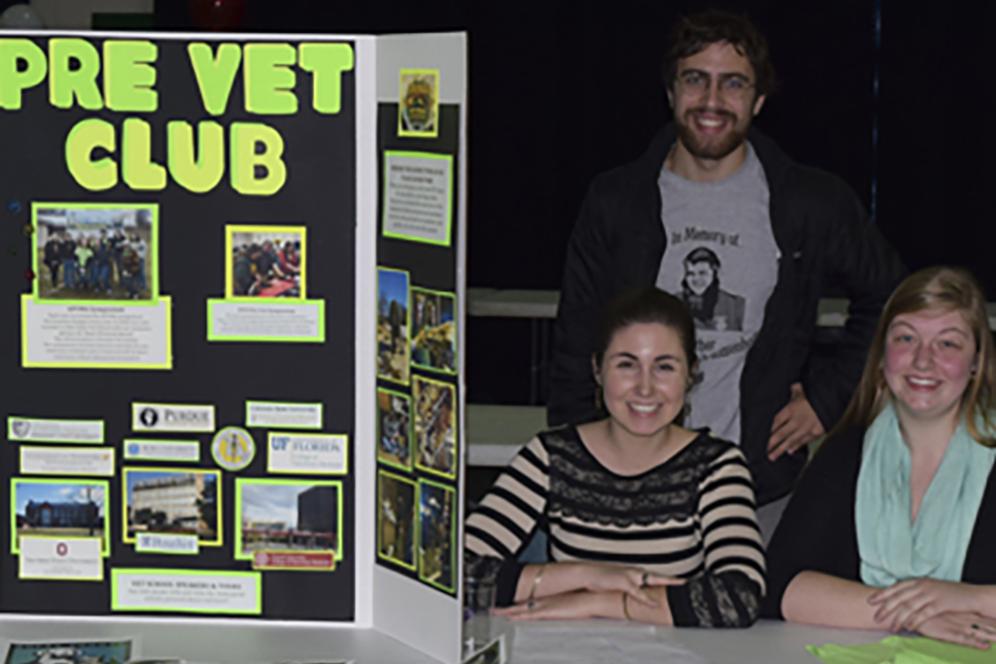 Several students sitting at a desk with a large poster that reads "Pre-Vet Club"