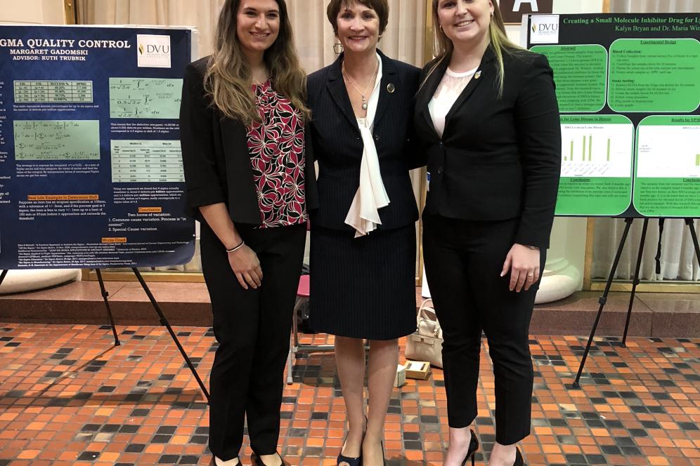 Two students from Delaware Valley University stand on either side of Marguerite Quinn in front of scientific posters.