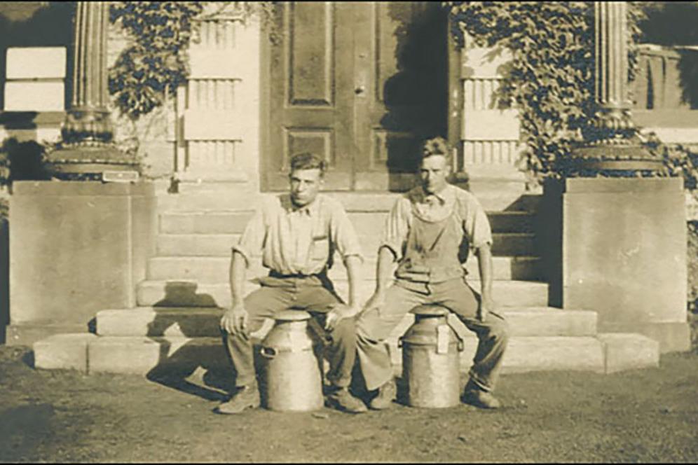 Two men sitting on large milk jugs.