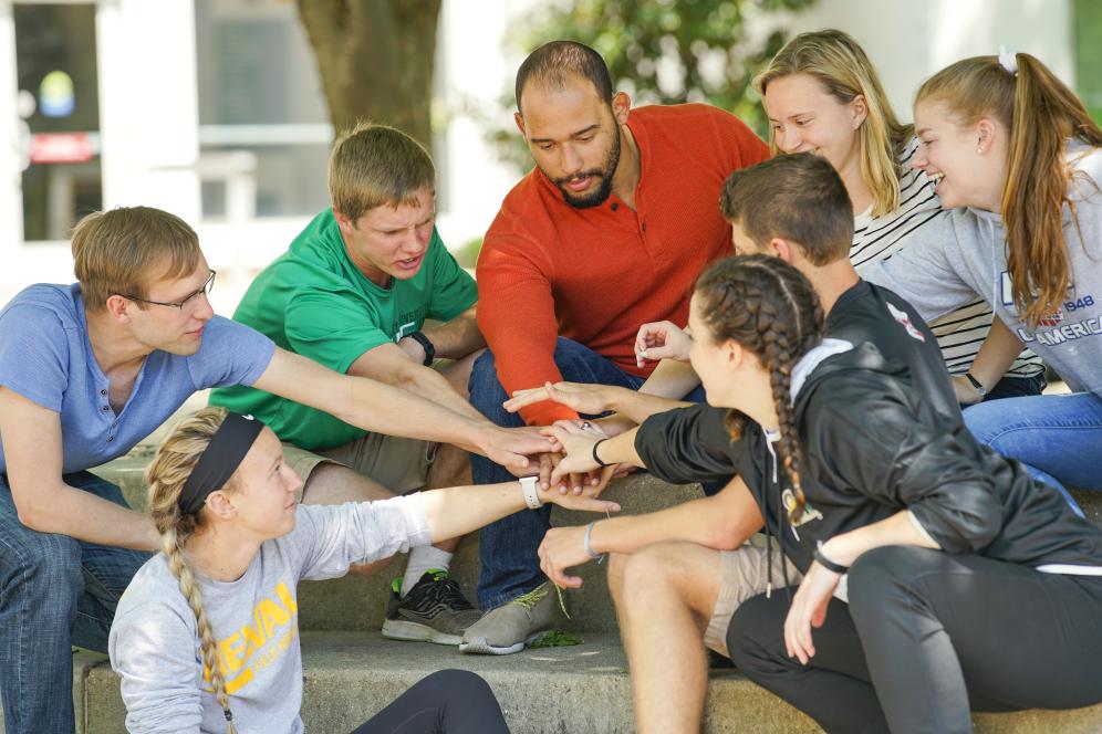 Faculty with group of students clasping hands