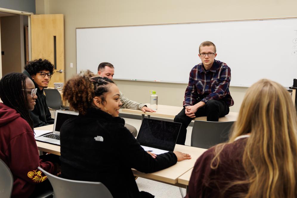 A group of students are sitting in class having a group conversation. 