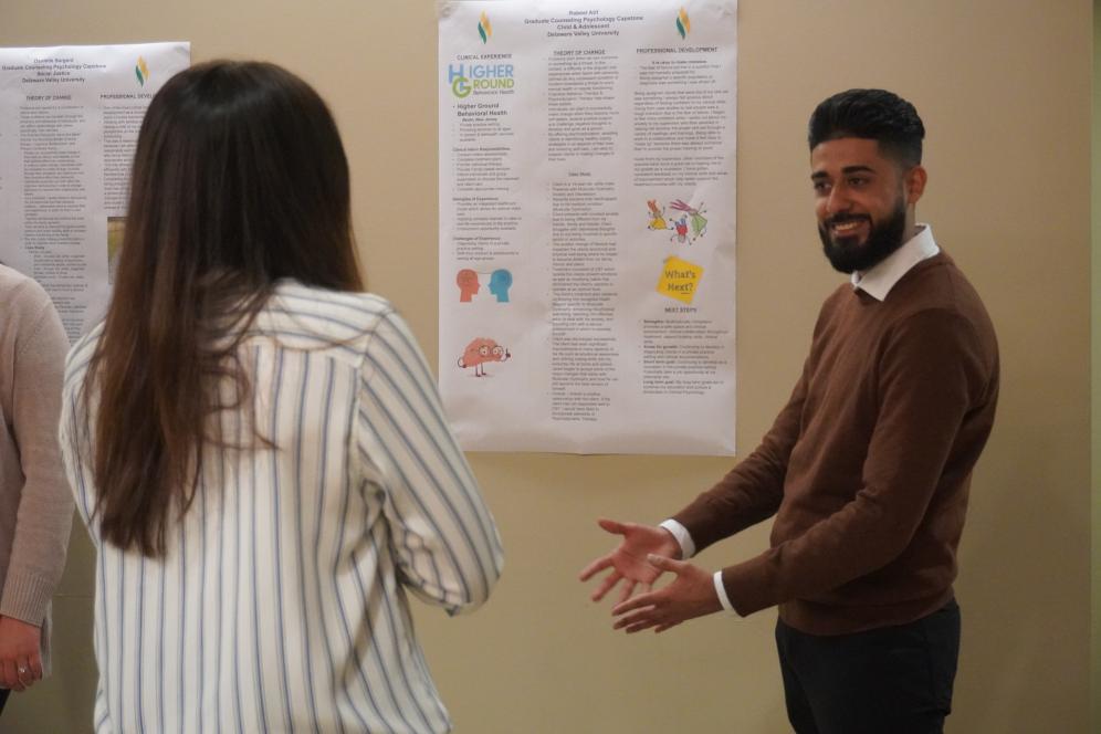 A male student is presenting his poster to a female visitor. 