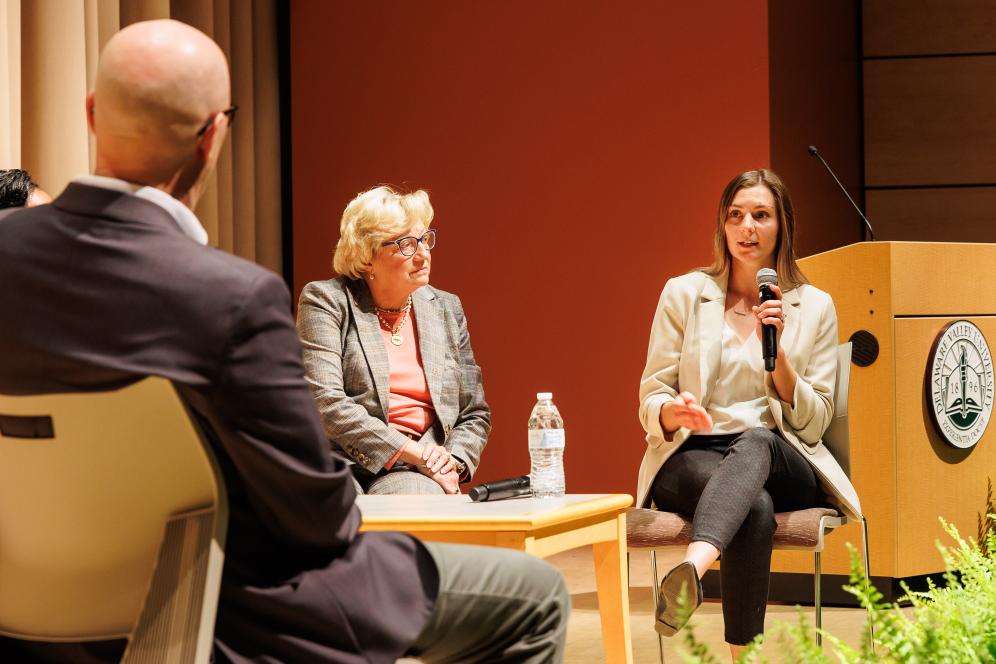 A female student is speaking on stage at a panel discussion event. 