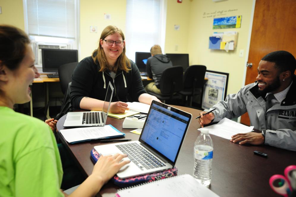 Students are seated at a table with laptops at the writing center. 