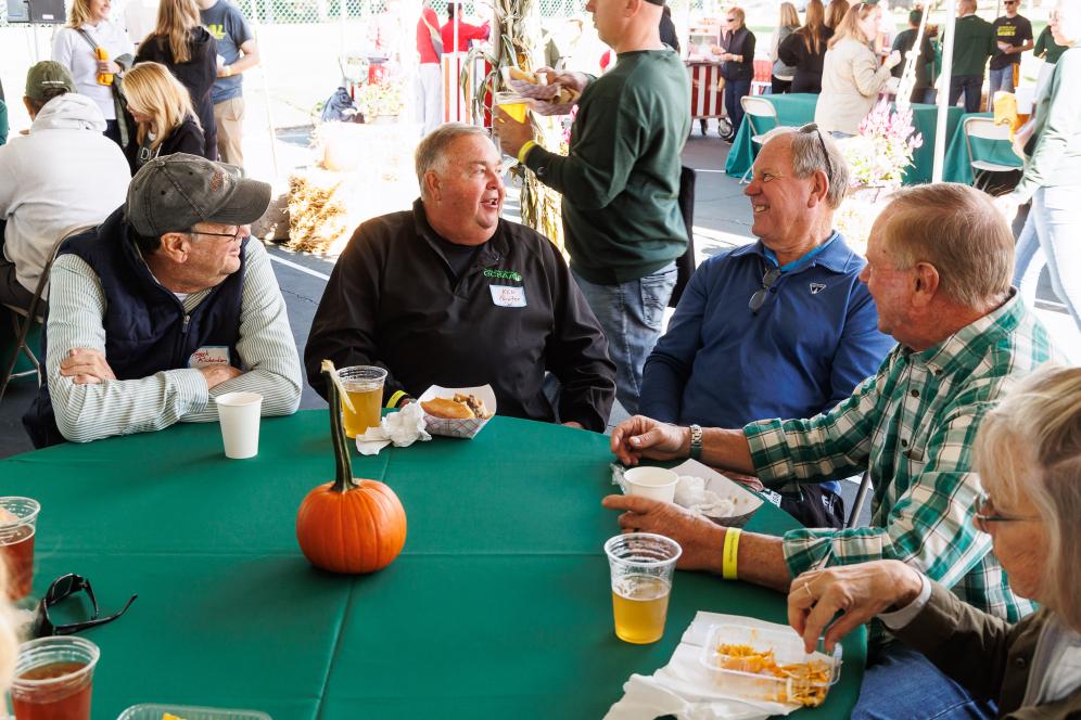 Alumni gather around a table with drinks and food at the homecoming tailgate. 
