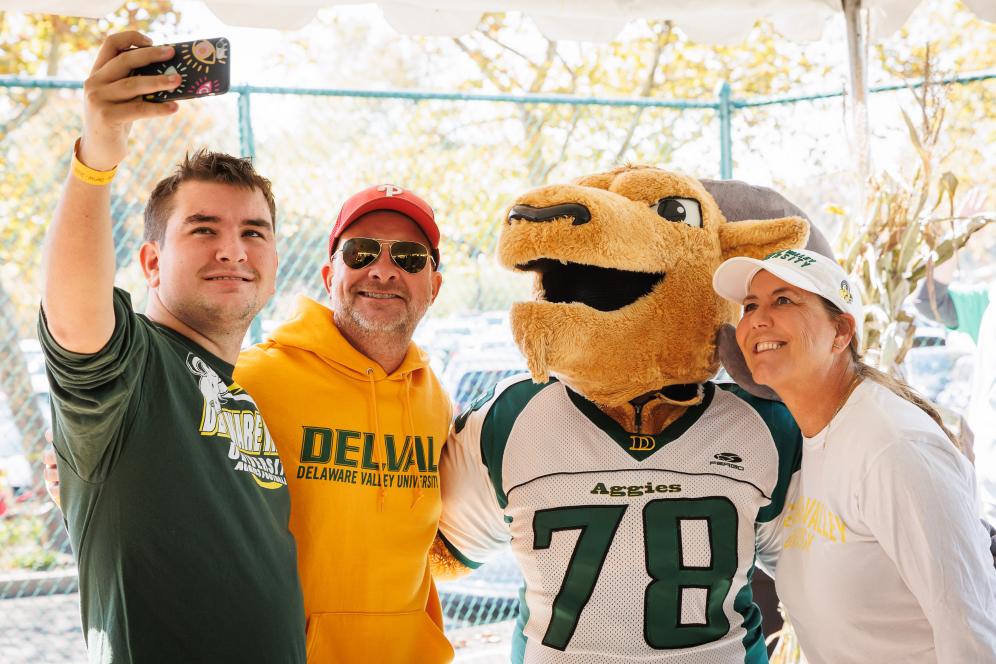 Three alumni pose for a photo with Caesar the mascot.