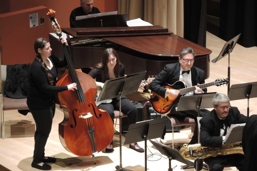 A student playing the cello while standing on stage.