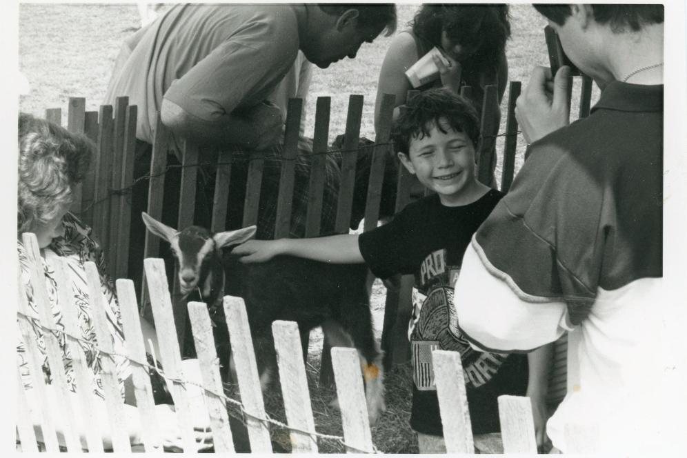 A child is petting a goat at aday in a historic black and white photo. 