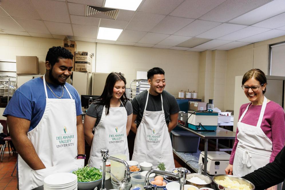 Laura Herbst is with three students in the food lab, and all are wearing aprons.